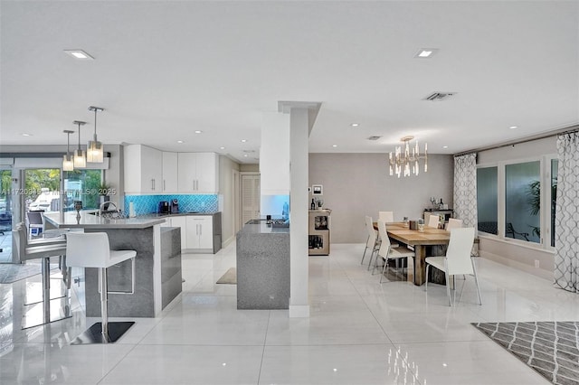 kitchen featuring sink, hanging light fixtures, a notable chandelier, white cabinets, and decorative backsplash