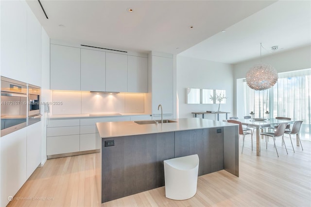 kitchen featuring white cabinets, a center island with sink, sink, hanging light fixtures, and light hardwood / wood-style floors