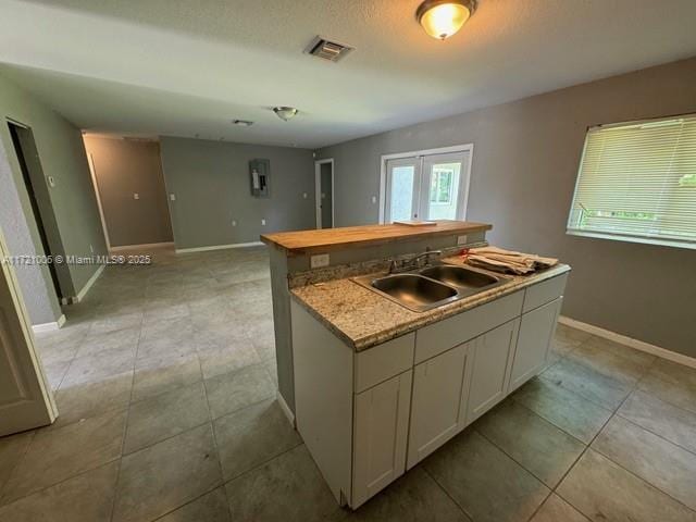 kitchen featuring white cabinetry, sink, french doors, a textured ceiling, and a kitchen island with sink