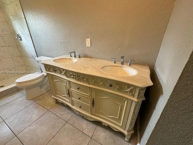 bathroom featuring tile patterned floors, vanity, a tile shower, and toilet