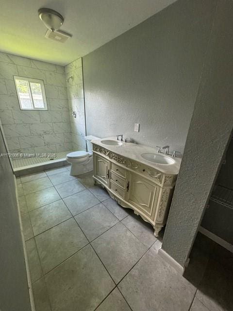 bathroom with tile patterned flooring, vanity, toilet, and tiled shower