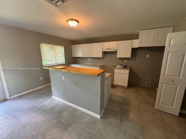 kitchen with a center island, white cabinets, a textured ceiling, and wood counters