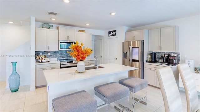 kitchen with stainless steel appliances, tasteful backsplash, an island with sink, white cabinets, and a kitchen bar