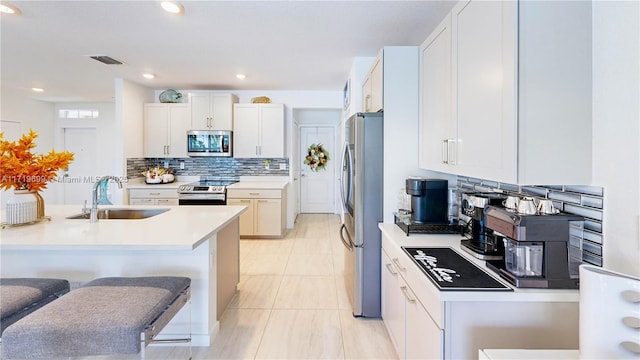 kitchen with sink, a breakfast bar area, stainless steel appliances, tasteful backsplash, and white cabinets