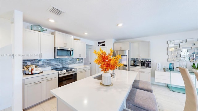 kitchen with a kitchen island, tasteful backsplash, white cabinets, a kitchen bar, and stainless steel appliances