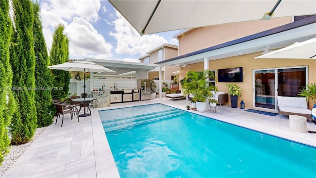 view of pool with exterior kitchen, a patio, sink, and ceiling fan