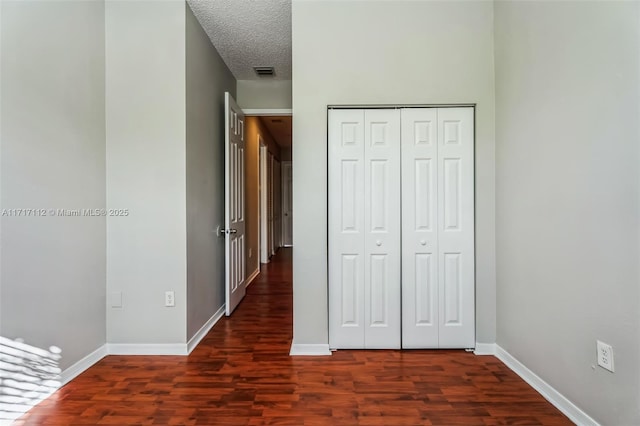 unfurnished bedroom featuring a closet, a textured ceiling, and dark wood-type flooring