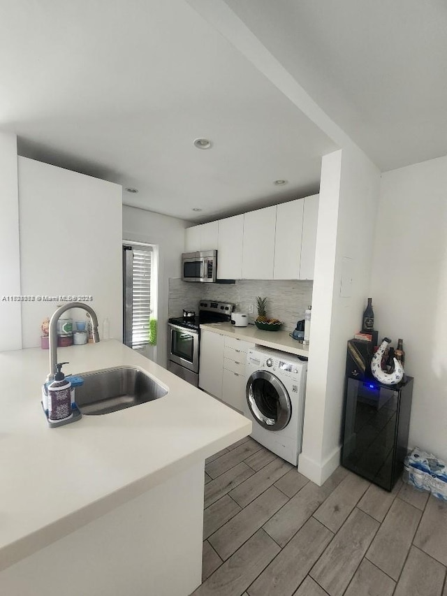 kitchen featuring backsplash, stainless steel appliances, sink, white cabinets, and washer / clothes dryer