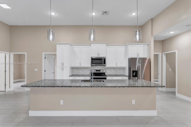 kitchen with appliances with stainless steel finishes, hanging light fixtures, an island with sink, and white cabinets