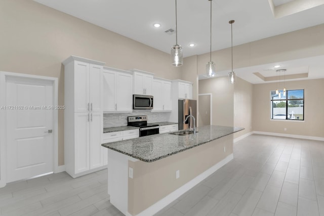 kitchen with stainless steel appliances, white cabinets, decorative light fixtures, stone counters, and a kitchen island with sink