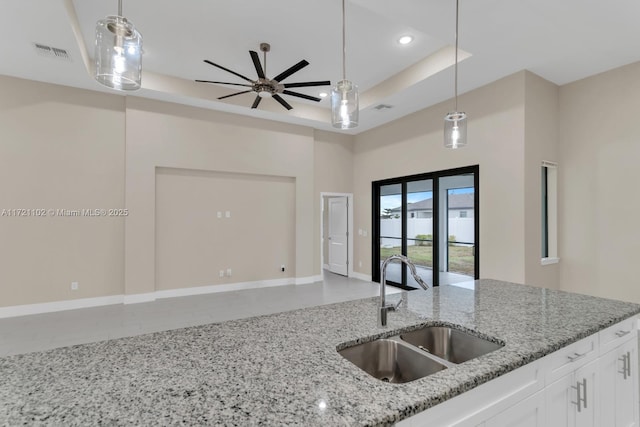 kitchen with light stone countertops, a tray ceiling, white cabinets, ceiling fan, and sink