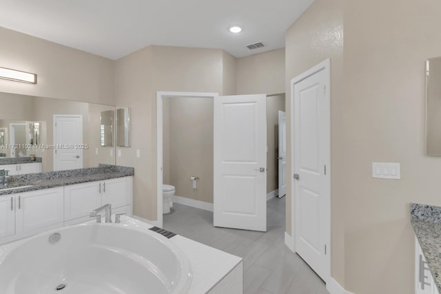 bathroom featuring toilet, a relaxing tiled tub, and vanity