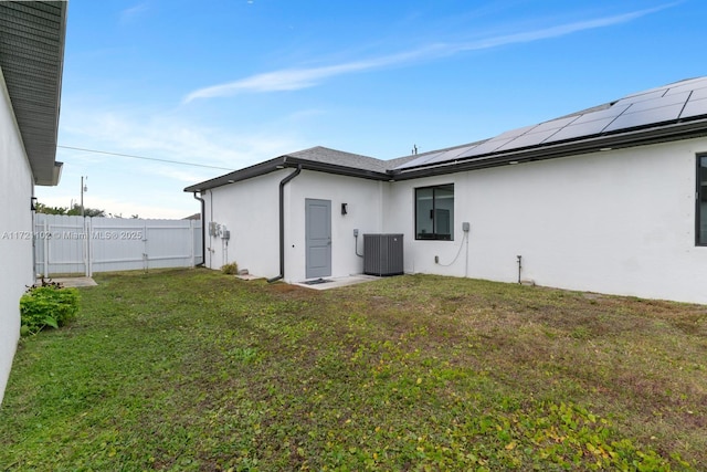 rear view of property with central air condition unit, solar panels, and a yard