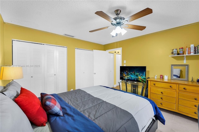 bedroom with light tile patterned flooring, a textured ceiling, ceiling fan, and two closets