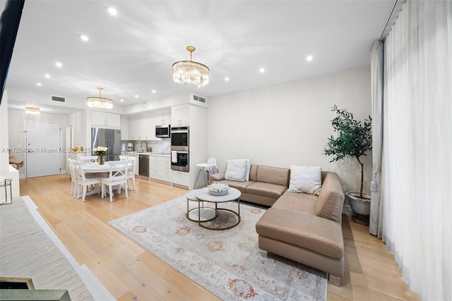 living room with light hardwood / wood-style flooring, a chandelier, and sink