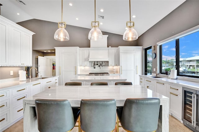 kitchen featuring wine cooler, backsplash, lofted ceiling, decorative light fixtures, and a breakfast bar area