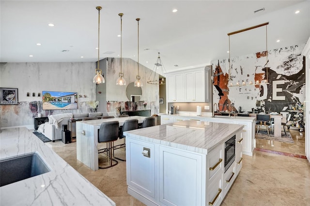 kitchen with white cabinets, hanging light fixtures, built in microwave, a large island, and light stone counters