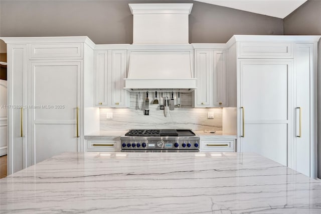 kitchen with high end range, light stone countertops, custom range hood, vaulted ceiling, and white cabinetry