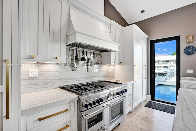 kitchen with white cabinetry, light stone counters, range with two ovens, and custom exhaust hood