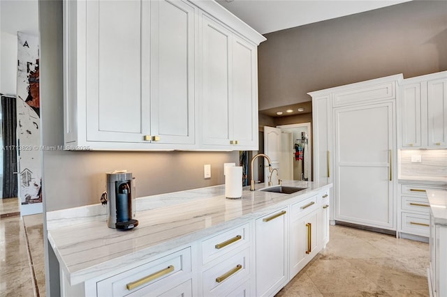 kitchen featuring white cabinets, light stone counters, and sink