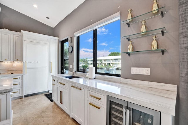 kitchen with backsplash, white cabinetry, wine cooler, and light stone counters