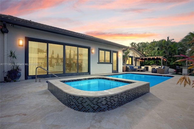 pool at dusk featuring an in ground hot tub, outdoor lounge area, and a patio area