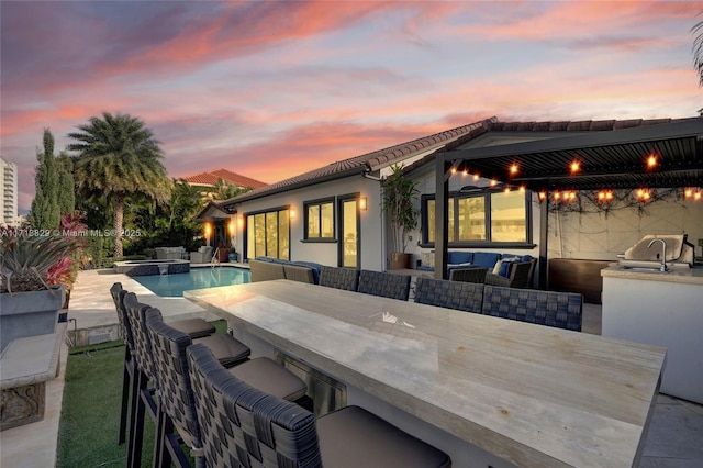 pool at dusk with an outdoor hangout area, area for grilling, and an outdoor wet bar