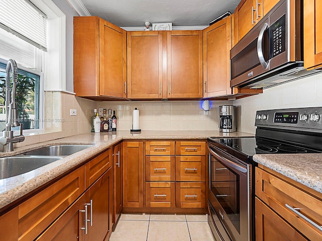 kitchen featuring sink, light stone countertops, light tile patterned floors, ornamental molding, and stainless steel appliances