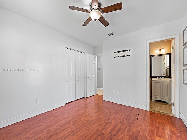 unfurnished bedroom featuring connected bathroom, ceiling fan, a closet, and wood-type flooring