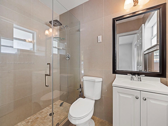 bathroom with vanity, toilet, tile walls, and a shower with shower door