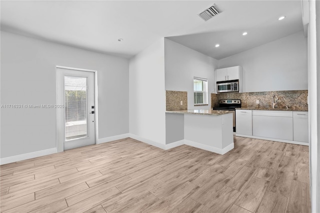 kitchen with kitchen peninsula, decorative backsplash, light stone countertops, stainless steel appliances, and white cabinetry