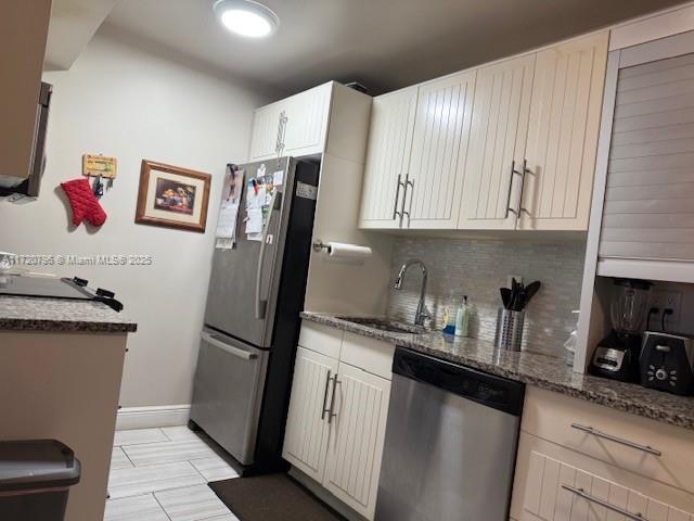 kitchen with white cabinetry, sink, stainless steel appliances, tasteful backsplash, and dark stone counters