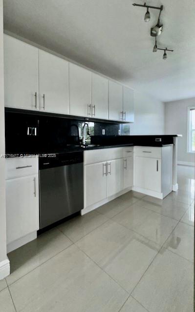 kitchen featuring stainless steel dishwasher, white cabinets, light tile patterned floors, and sink