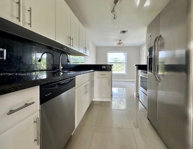 kitchen with stainless steel appliances, light tile patterned floors, dark stone counters, decorative backsplash, and white cabinets