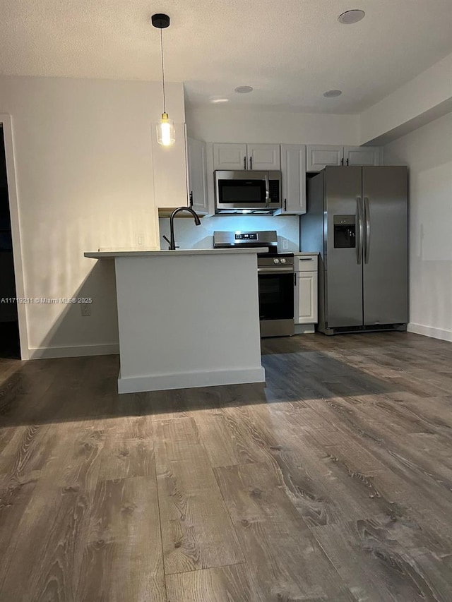 kitchen featuring pendant lighting, sink, dark hardwood / wood-style floors, appliances with stainless steel finishes, and kitchen peninsula