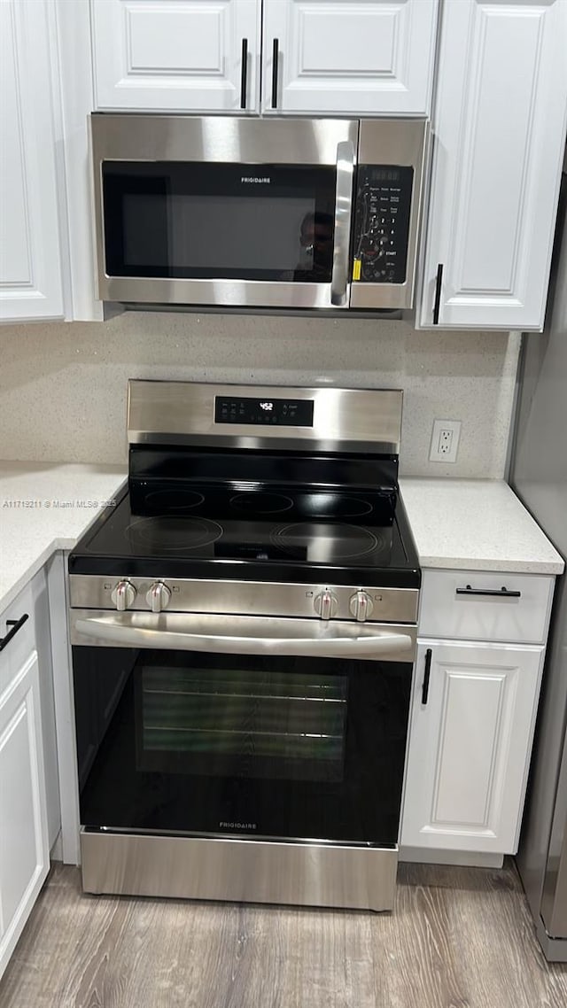 kitchen with white cabinets, appliances with stainless steel finishes, light hardwood / wood-style flooring, and light stone countertops