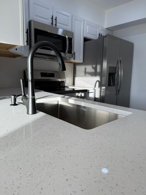 kitchen with white cabinets, black fridge with ice dispenser, and light stone counters