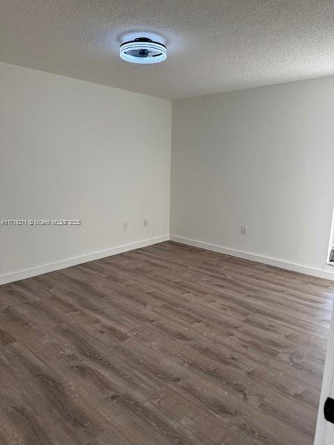 unfurnished room with a textured ceiling and dark wood-type flooring