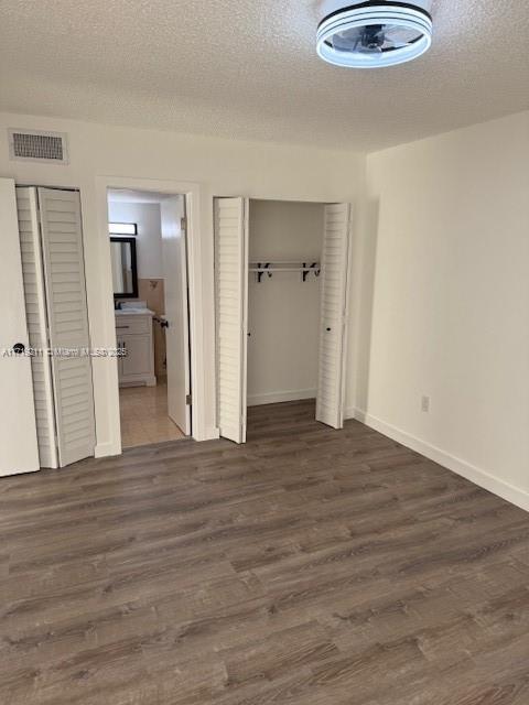 unfurnished bedroom featuring a textured ceiling, ensuite bathroom, and dark wood-type flooring