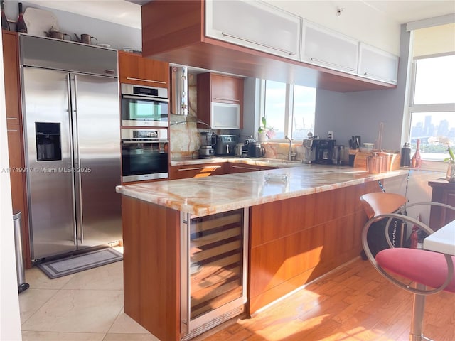 kitchen featuring sink, wine cooler, appliances with stainless steel finishes, light stone counters, and kitchen peninsula