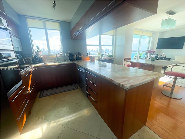 kitchen with wall oven, stainless steel dishwasher, kitchen peninsula, dark brown cabinets, and light tile patterned floors