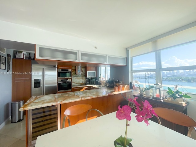 kitchen with light stone countertops, sink, beverage cooler, a water view, and appliances with stainless steel finishes