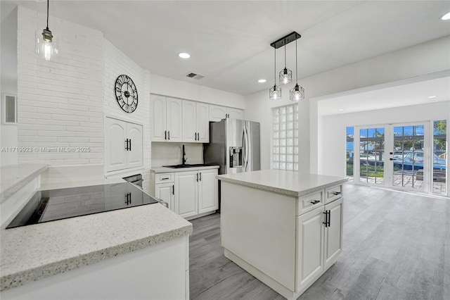 kitchen with white cabinetry, visible vents, light wood-type flooring, stainless steel fridge with ice dispenser, and decorative light fixtures