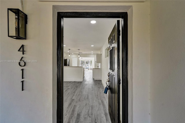 hall featuring light wood-style floors, recessed lighting, and baseboards