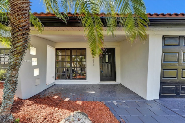 property entrance featuring a tiled roof, a porch, and stucco siding