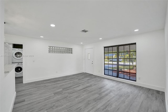 unfurnished room with recessed lighting, stacked washer and dryer, wood finished floors, visible vents, and baseboards