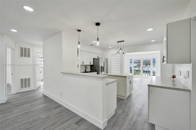 kitchen with a center island, visible vents, light wood-style flooring, and stainless steel fridge with ice dispenser