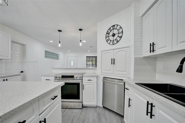 kitchen with pendant lighting, stainless steel appliances, a sink, and white cabinets