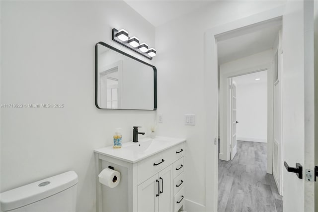 bathroom with wood finished floors, vanity, toilet, and baseboards