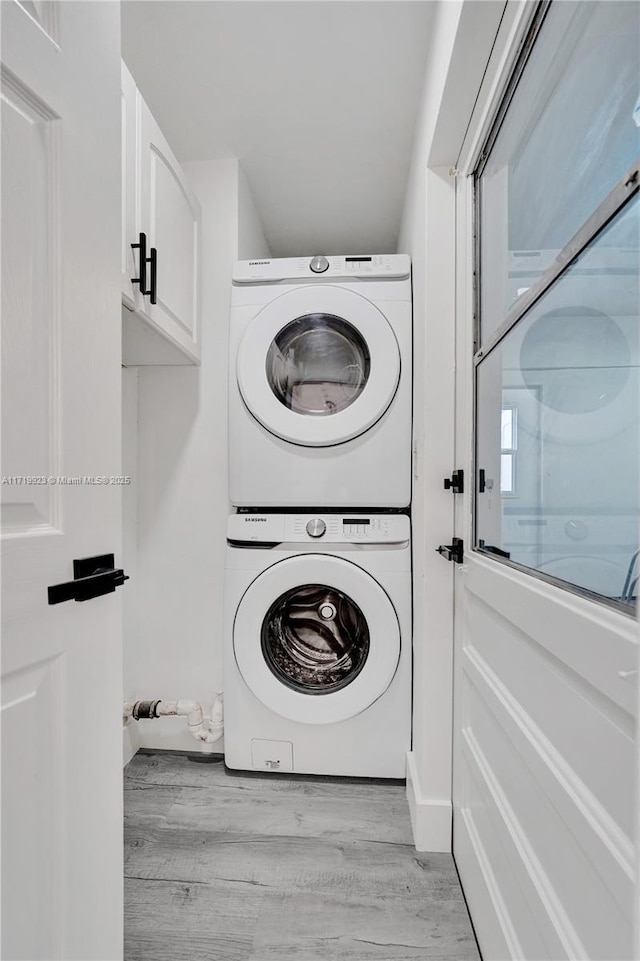 laundry area featuring cabinets, a healthy amount of sunlight, light hardwood / wood-style floors, and stacked washer and clothes dryer